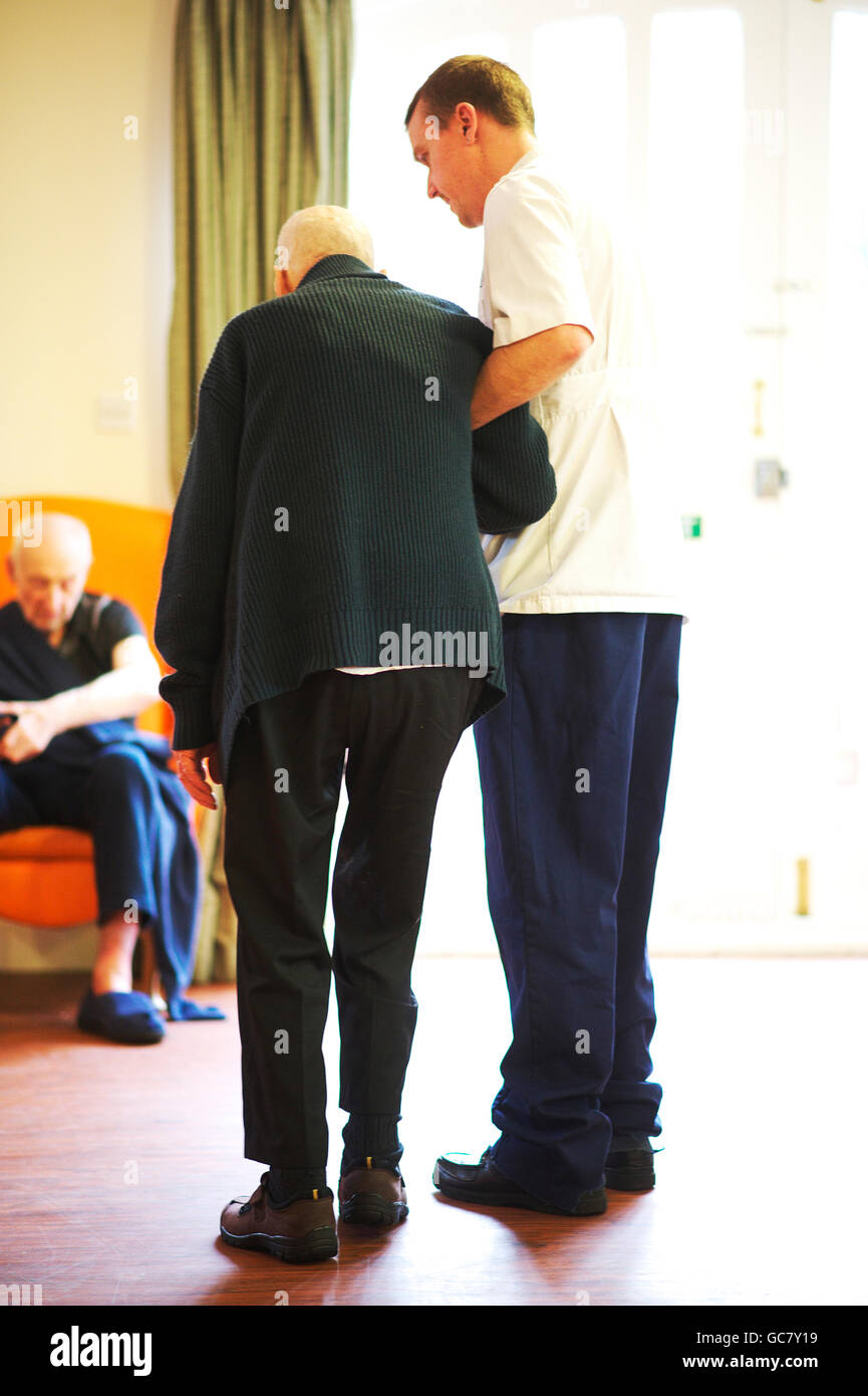 Elderly care home patient is helped by male nurse in the common space of the dementia home Stock Photo