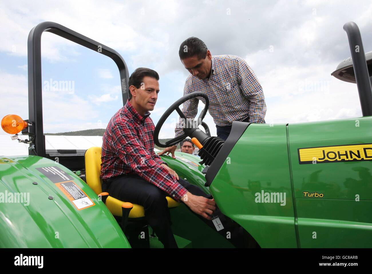 Mexican President Enrique Pena Nieto, sitting, is shown how to operate a John Deere tractor by Michoacan Governor Silvano Aureoles during a ceremony to deliver 600 farm tractors to poor farmers July 5, 2016 in La Goleta, Charo, Michoacan, Mexico. The government program plans to provide 25,000 tractors to poor farmers by 2018 in the hope of improving agricultural production across the nation. Stock Photo