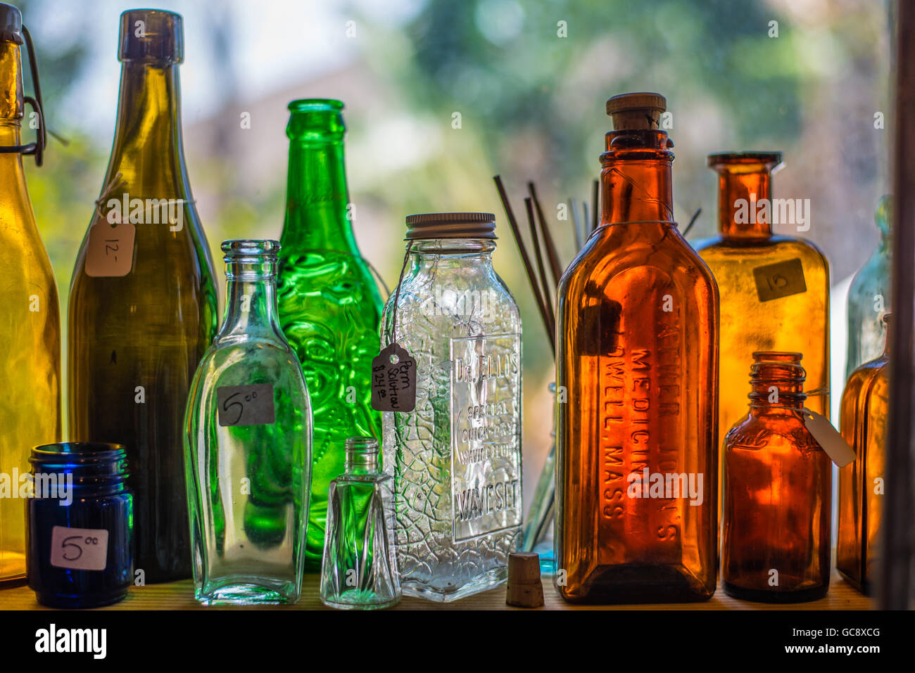 Vintage colored glass bottles on a window sill for sale at an antique shop Stock Photo
