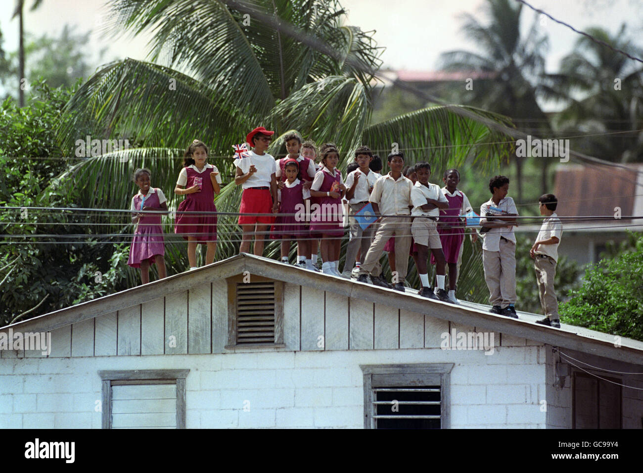 Schoolchildren find a vantage point on a rooftop as they watch for the Queen and Duke of Edinburgh during a visit to the provincial town of San Ignacio on a visit to Belize. Stock Photo