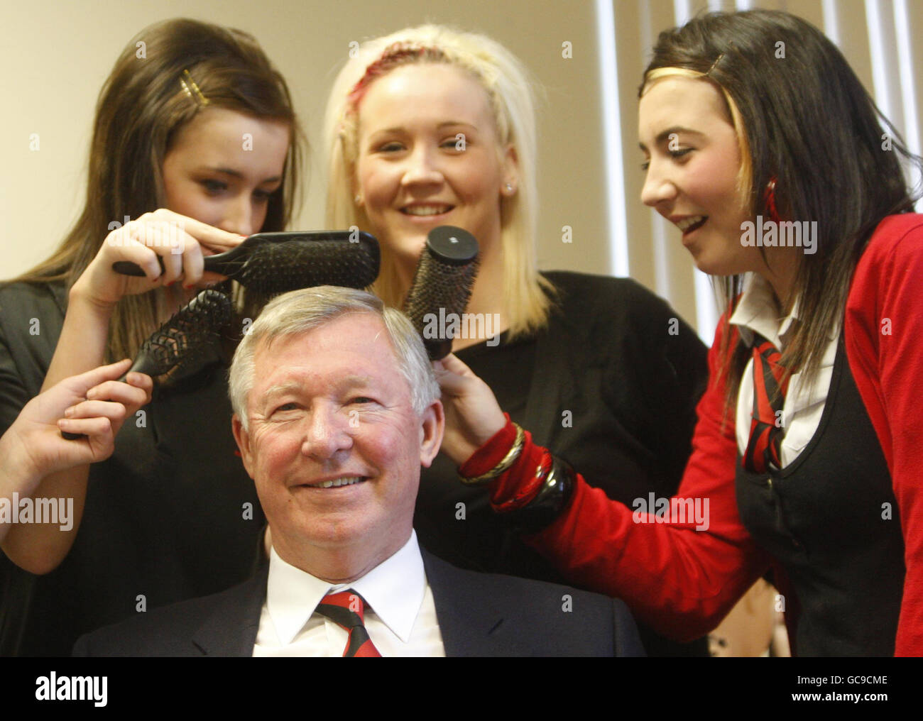Manchester United manager Sir Alex Ferguson with students (left to right) Nicola Hunter, Emma Hanley and Mairead Linning, during a visit to the hair dressing department in his former school, Govan High School, which this year celebrates its 100th anniversary. Stock Photo