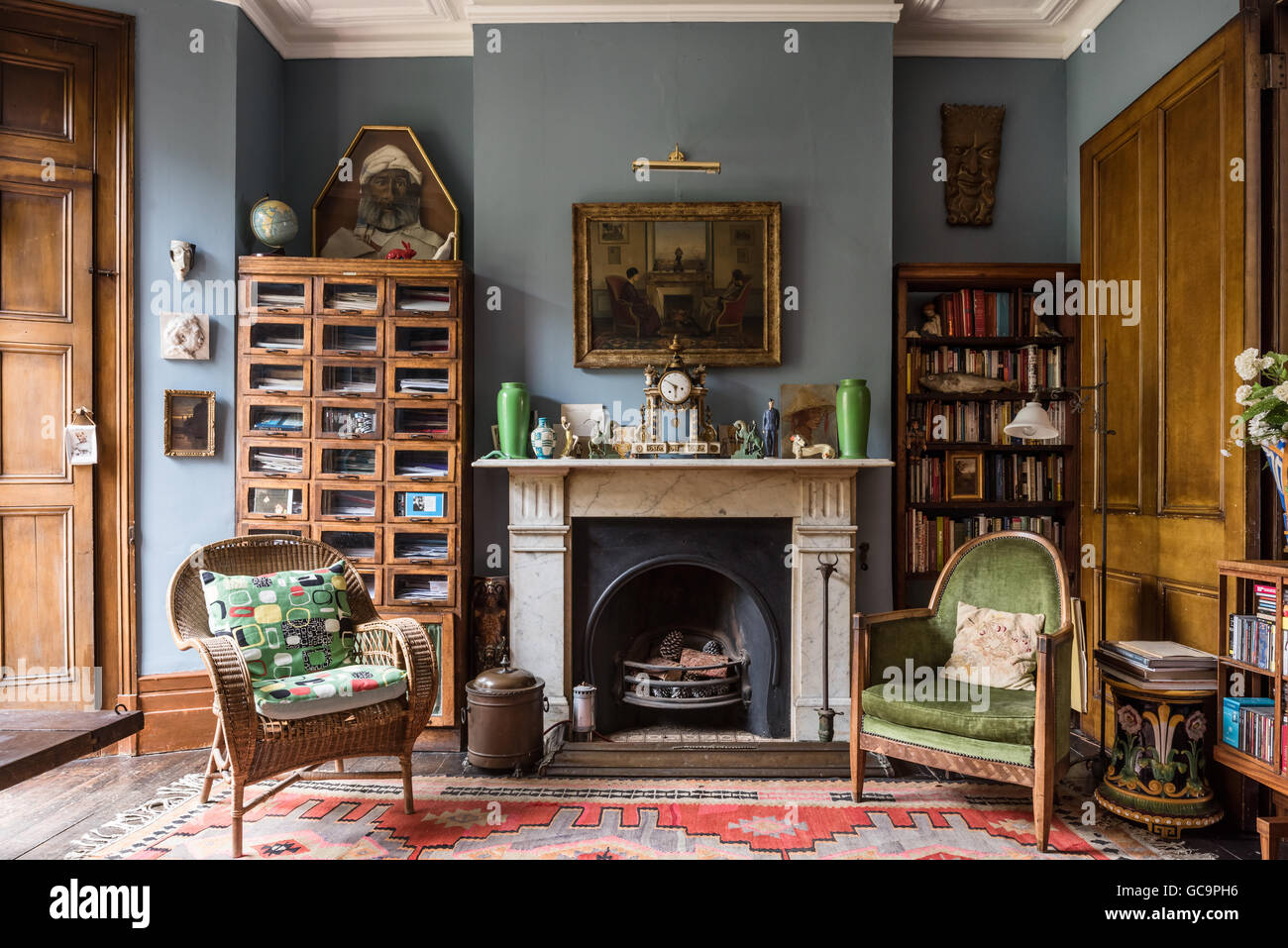 1930s drapers storage unit with colonial clock and chair and velvet upholstered open armchair in Nottinghill home, London, UK Stock Photo