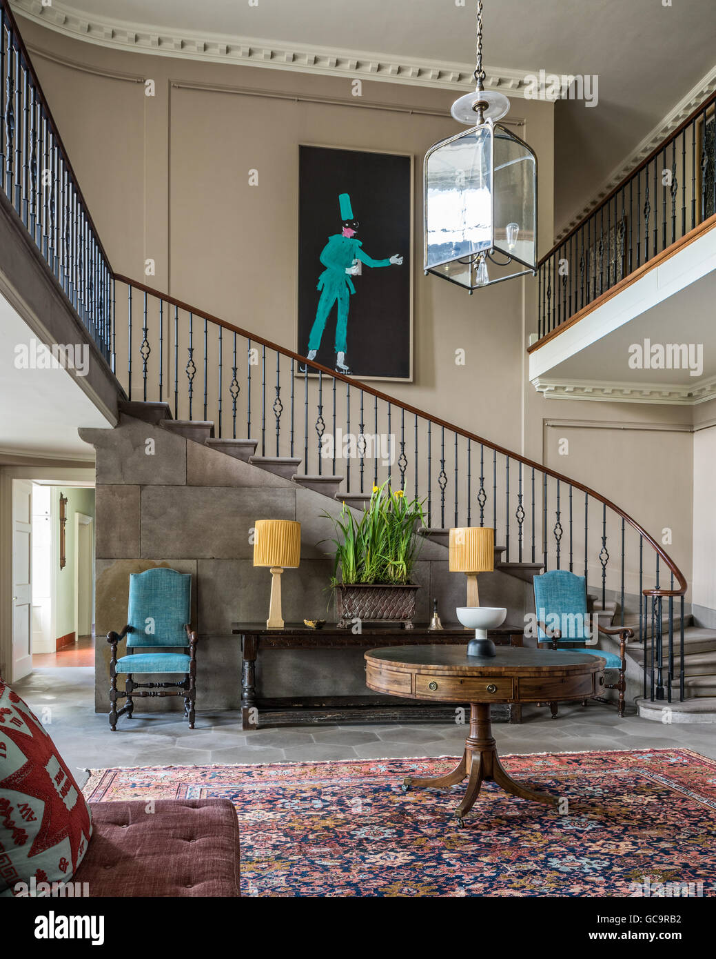 Fine curved stone staircase in entrance hall with large oriental carpet and David Hockney painting Stock Photo