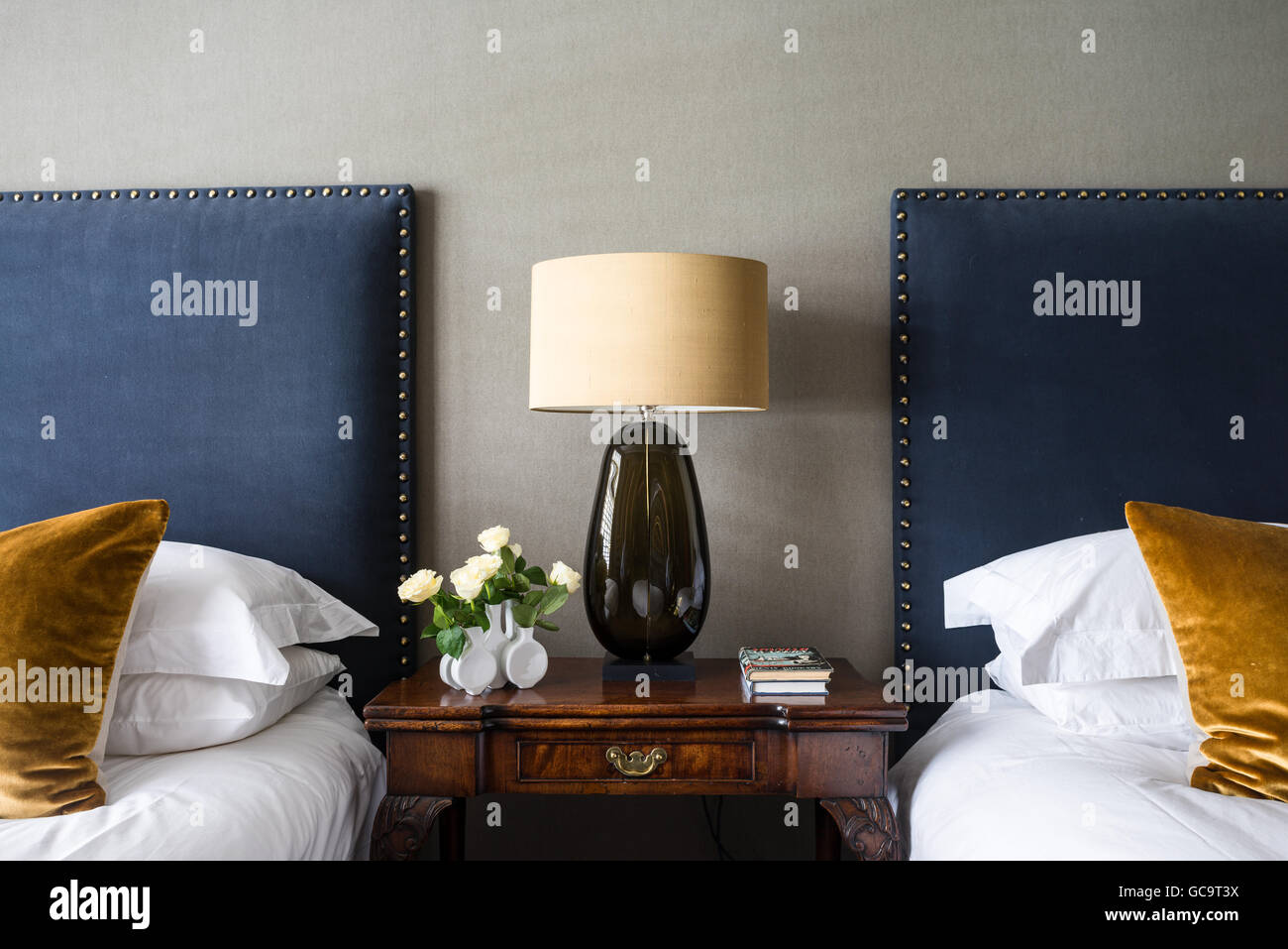 A Port Romana lamp in between twin beds with headboards covered in  Turnell & Gignon's Decortex Fizzy Stock Photo