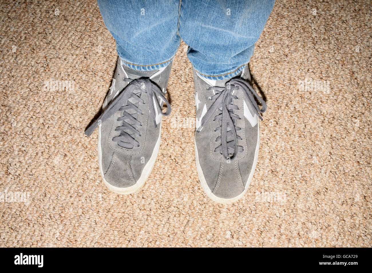 Close up of lower legs and feet of person wearing blue denim jeans and grey Converse trainers Stock Photo