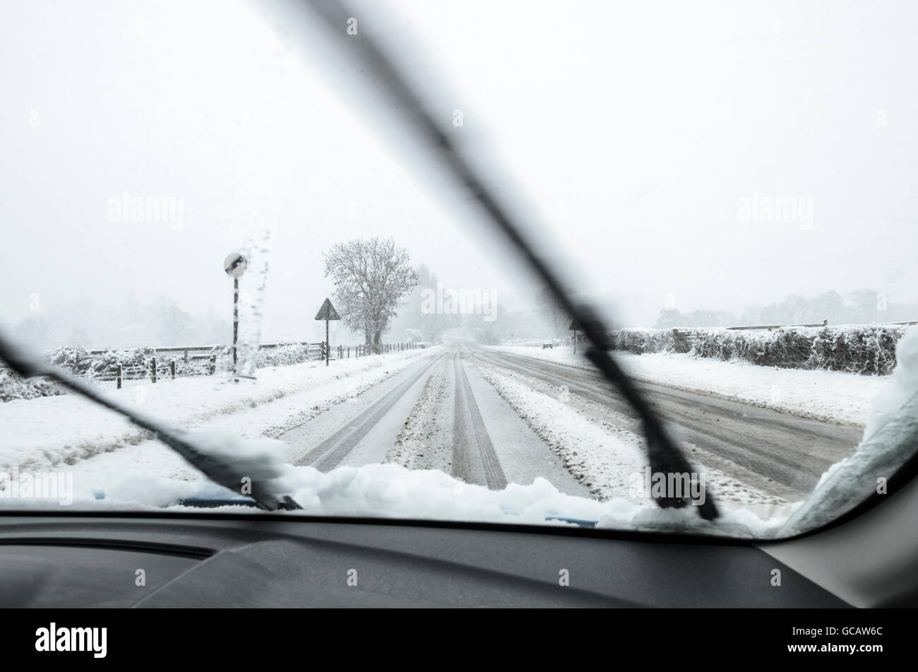 The view though the windscreen of a motor car being along a snow covered rural road. Stock Photo