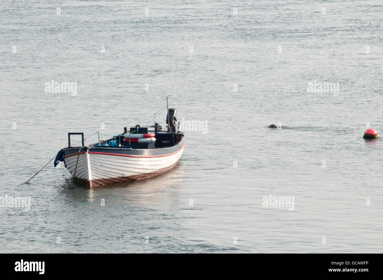 Small fishing boat at sunrise, moored in the water ready for sailing Stock Photo