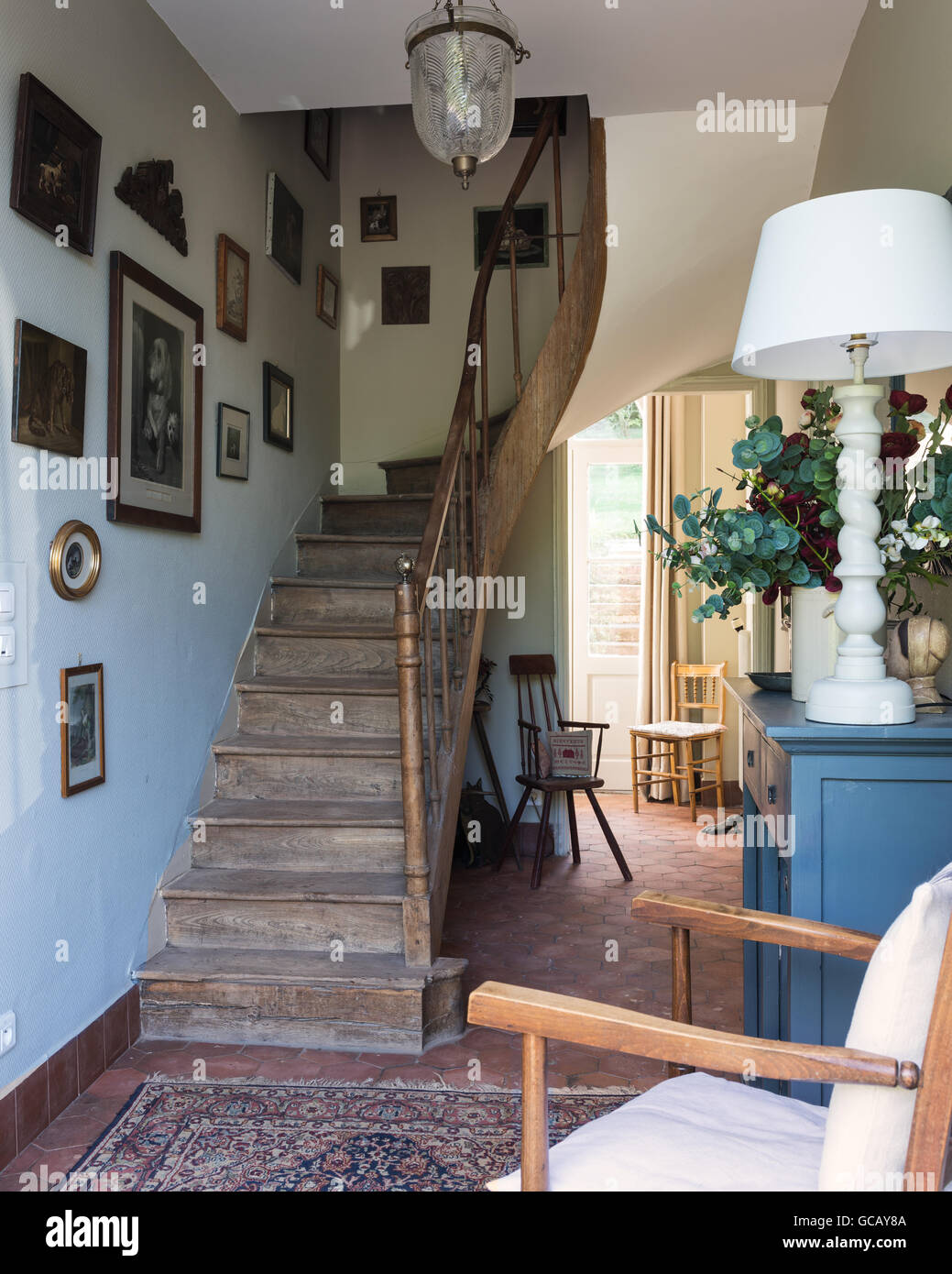 Entrance hall with terracotta floor tiles, wooden staircase and oriental rug Stock Photo