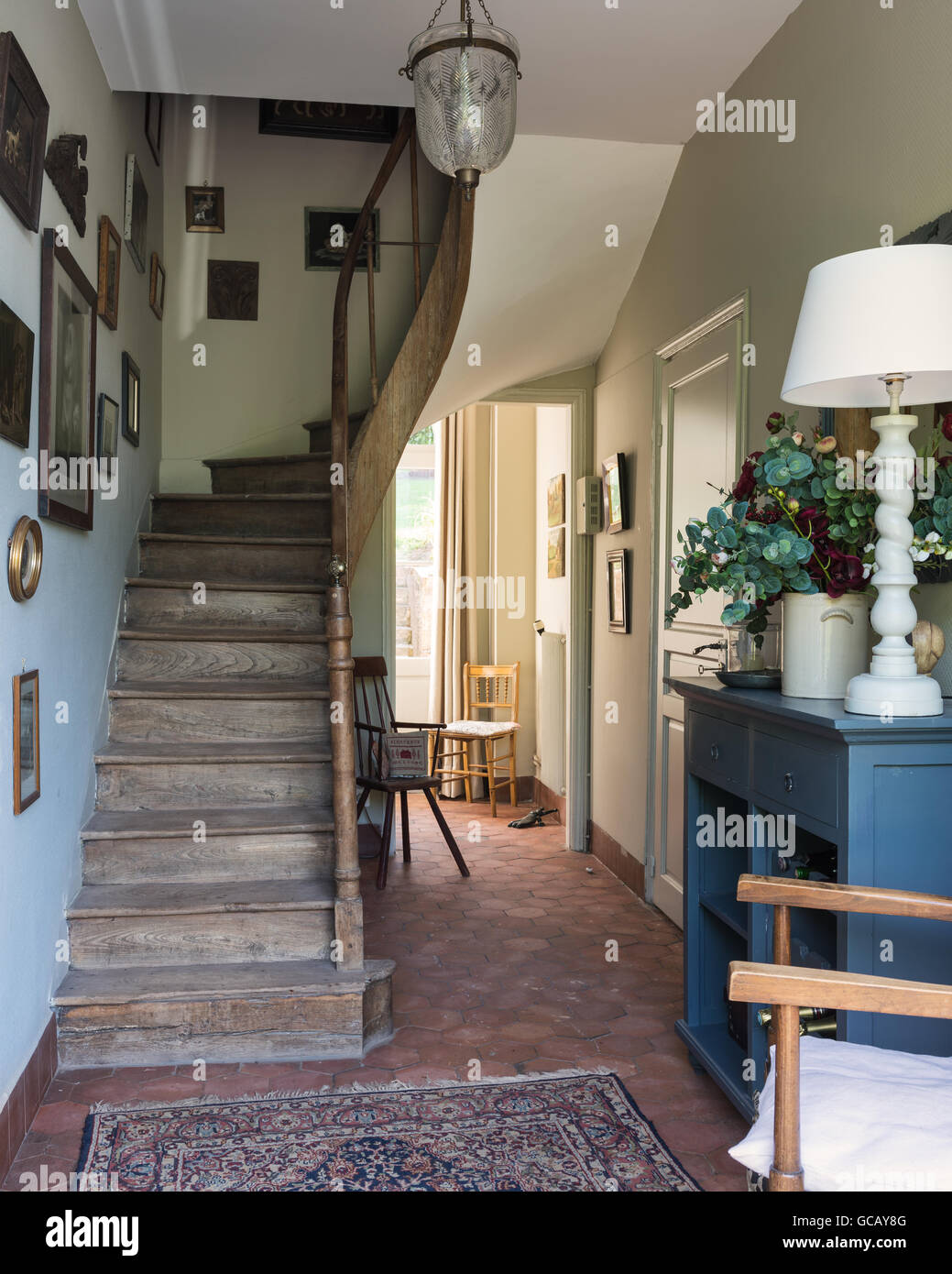 Entrance hall with terracotta floor tiles, wooden staircase and oriental rug Stock Photo