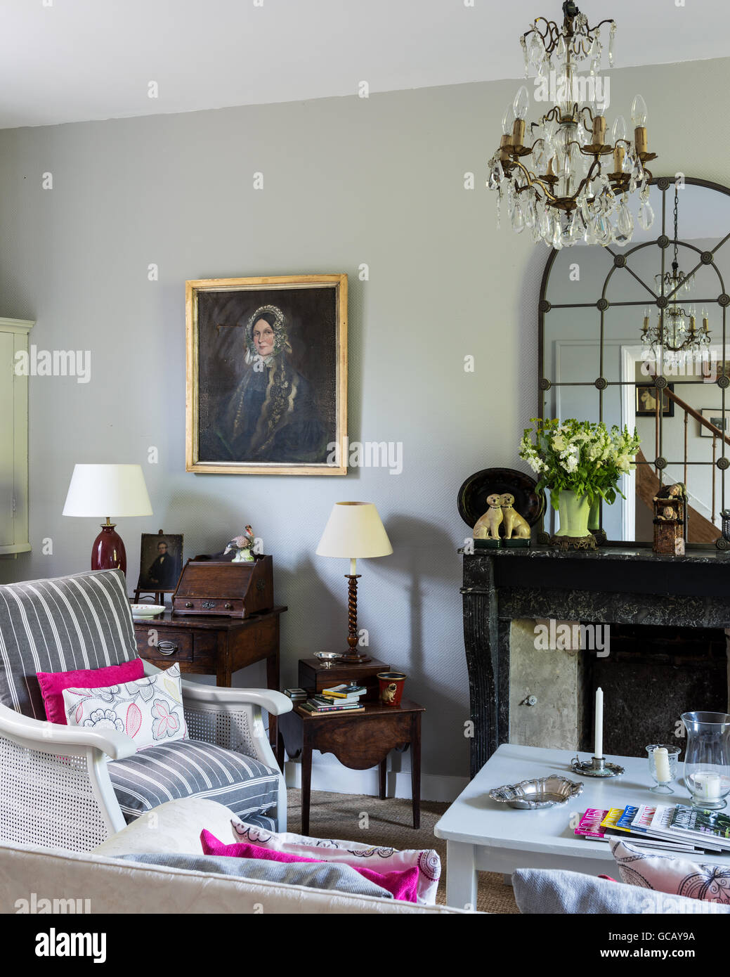 Light grey sitting room with crystal chandelier, oil painted portrait and striped upholstered armchairs Stock Photo