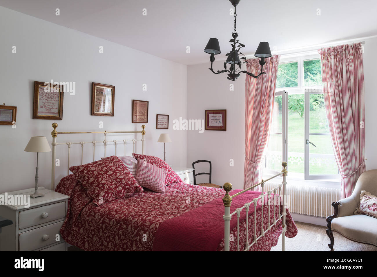 Victorian brass bed with red and white quilt. The curtains are Peony ticking by Ian Mankin Stock Photo