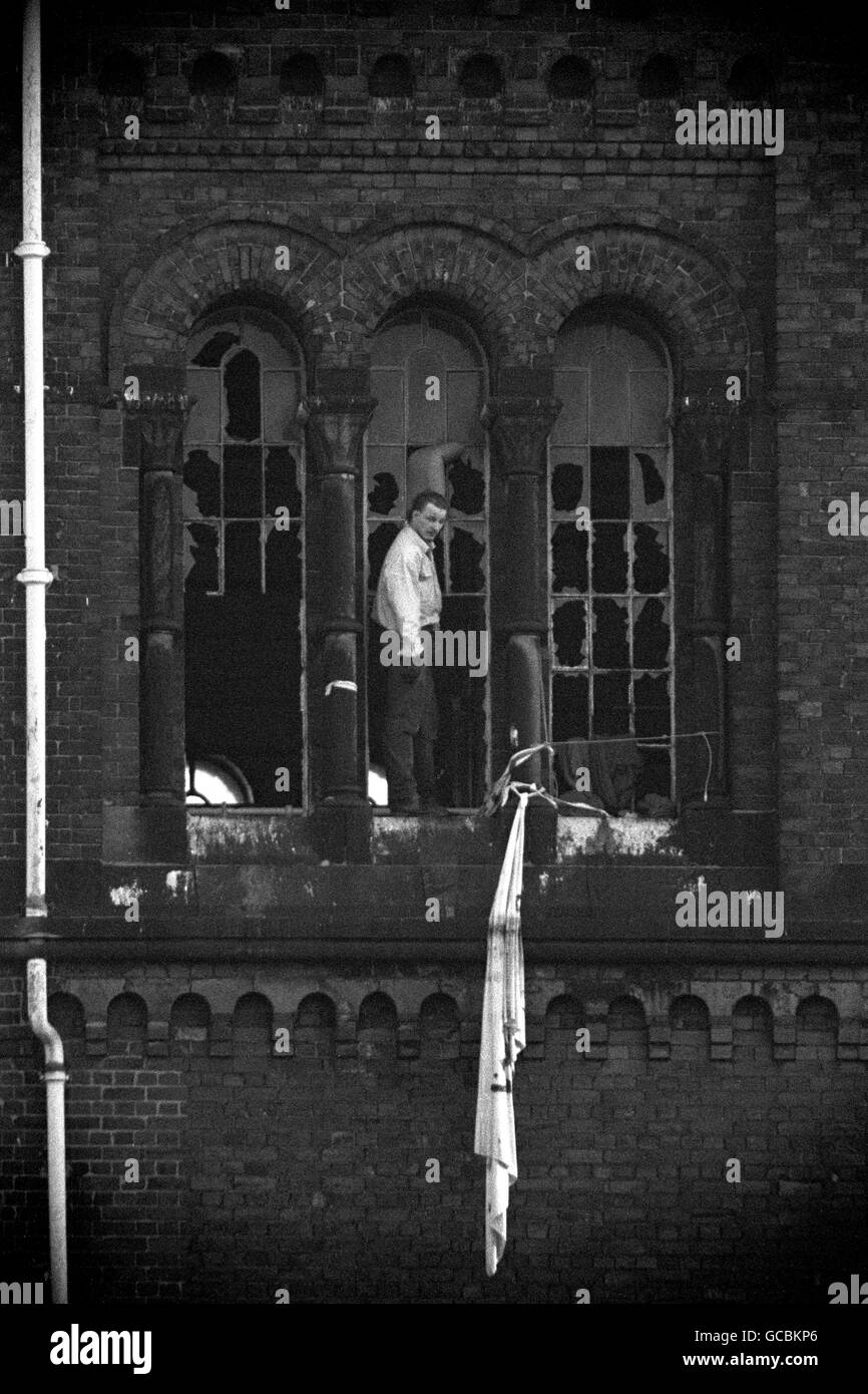 Prisoners' leader Paul Taylor makes a dawn appearance against the wrecked rotunda windows of Strangeways Prison in Manchester after fires were started by six inmates still barricaded inside. Stock Photo