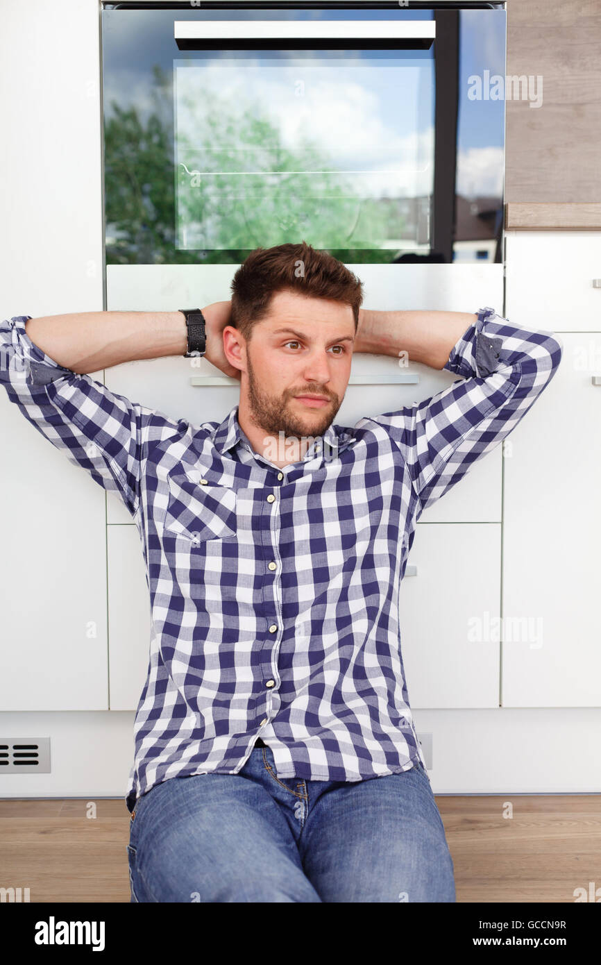 Attractive young man resting in a modern kitchen. Young man sitting leaning against the kitchen waiting for his girlfriend. Stock Photo