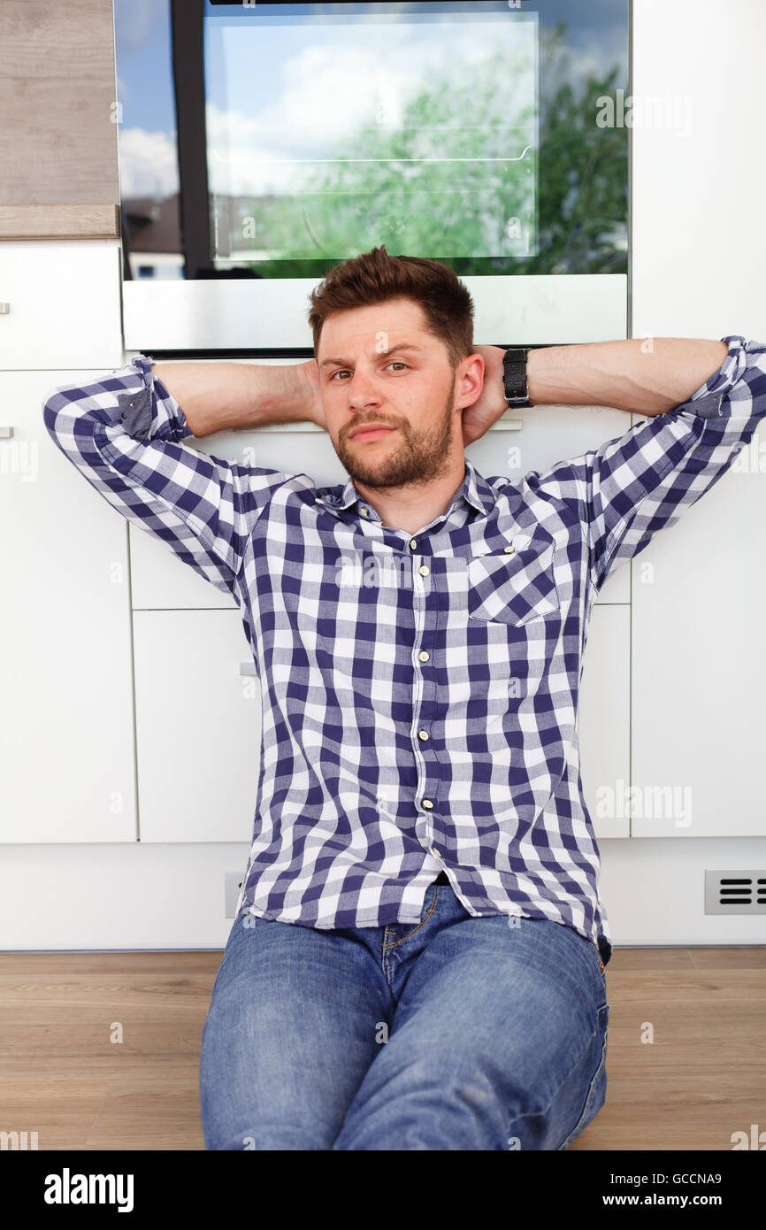 Attractive young man resting in a modern kitchen. Young man sitting leaning against the kitchen waiting for his girlfriend. Stock Photo