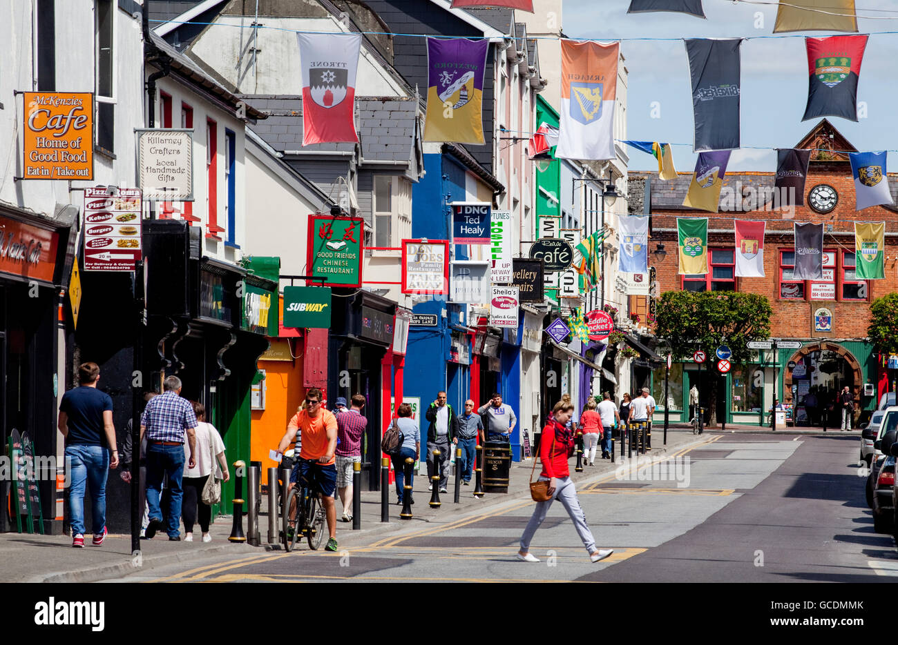 Pedestrians on the busy sidewalk with colourful buildings and banners with crests hanging over the street; Killarney, County Kerry, Ireland Stock Photo