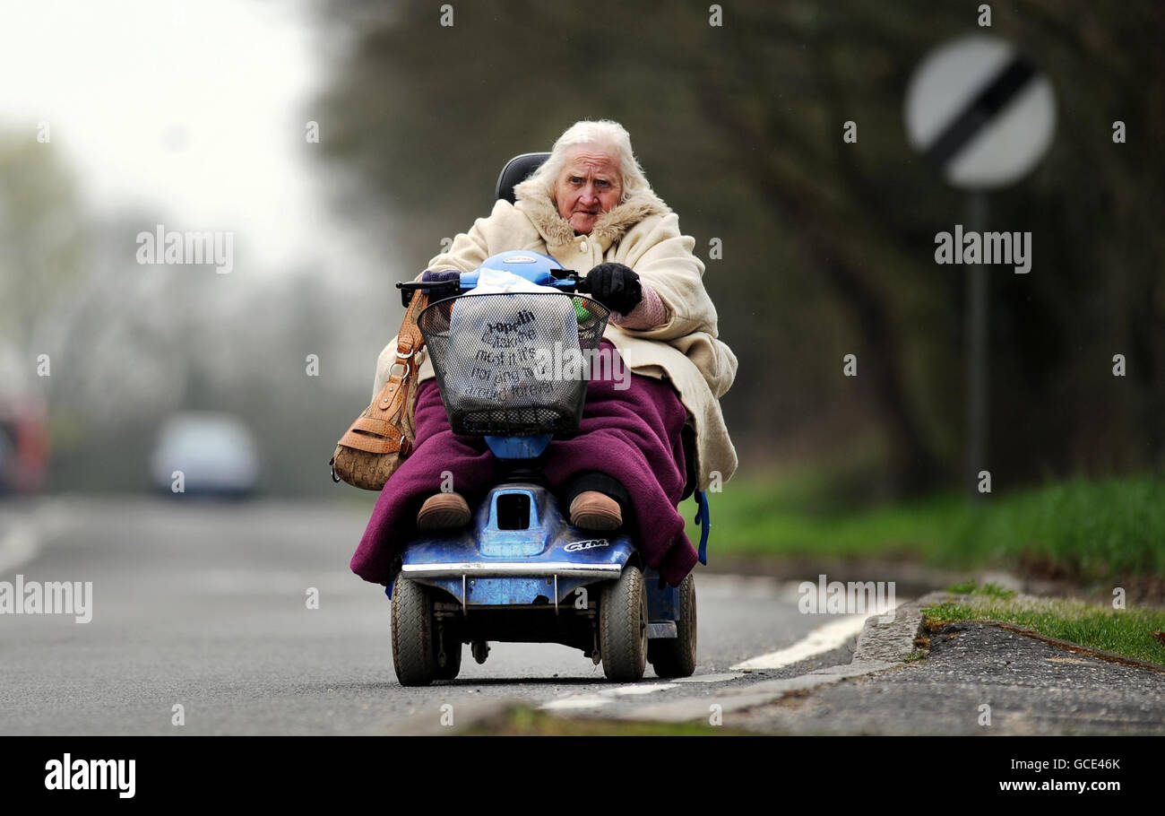 An elderly woman drives a mobility scooter along a national speed limit