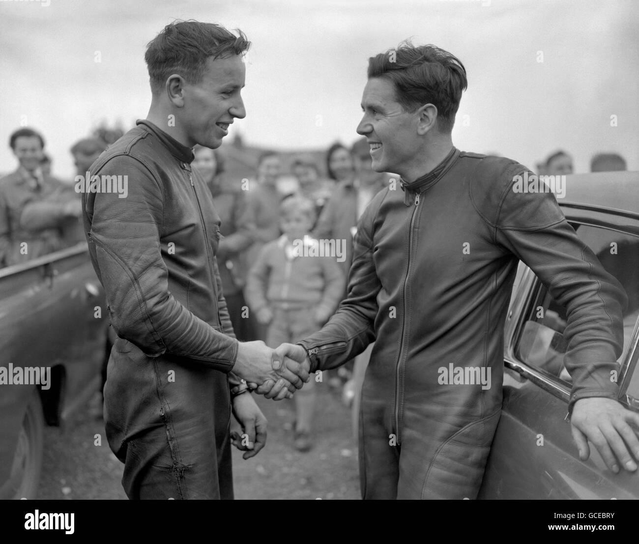World motorcycle champion, Geoff Duke (r), congratulates 21-year-old John Surtees after he was beaten by the youngster at Brands Hatch. Surtees, riding a Norton, triumphed in an exciting duel during the non-championship event. Stock Photo