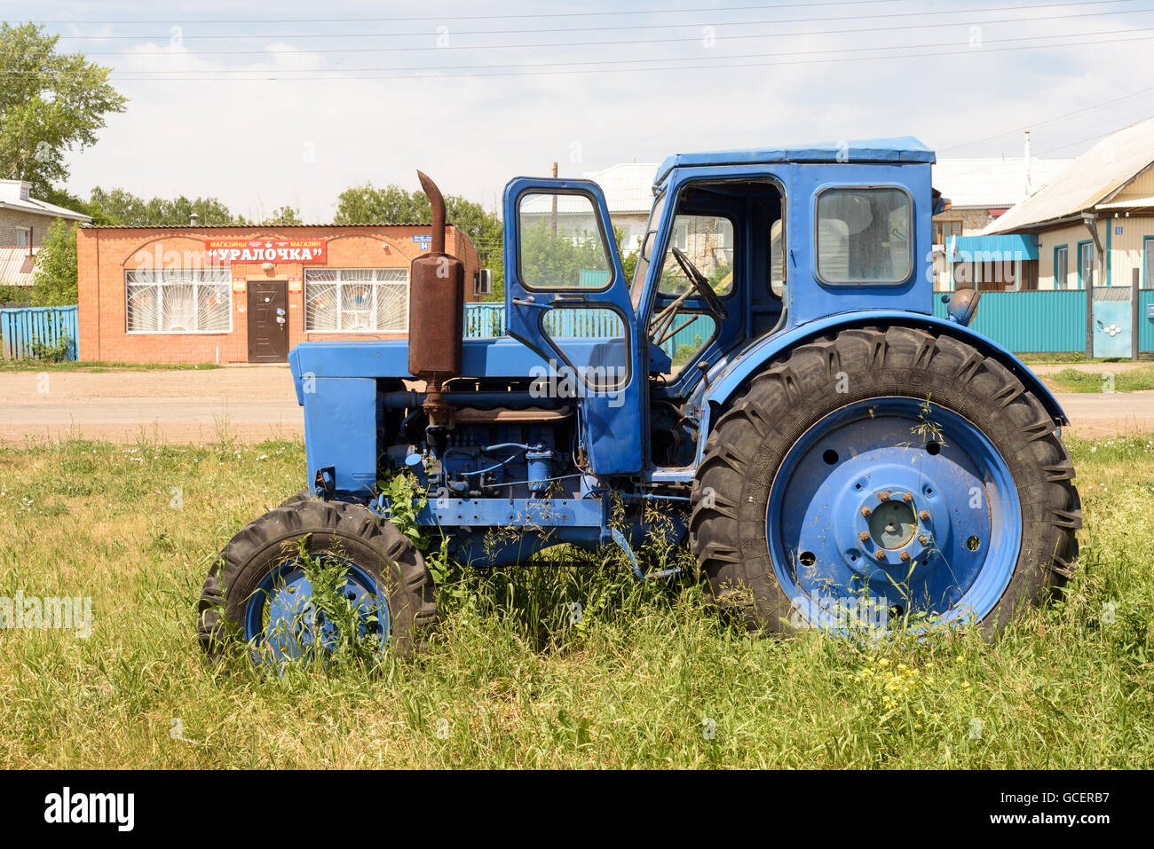 Single blue painted broken down tractor outside in sunlight Stock Photo