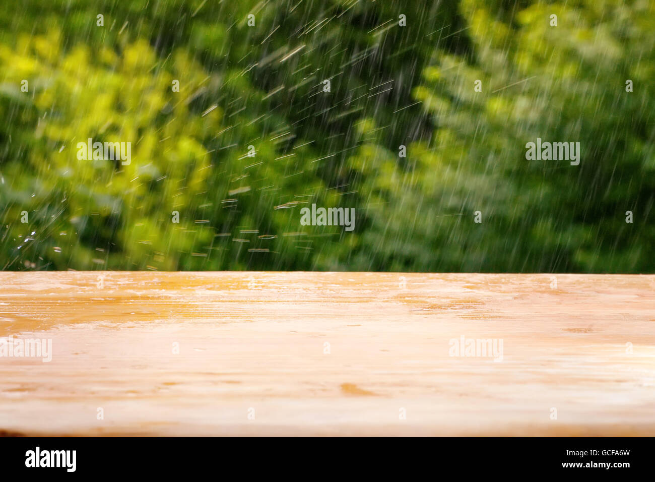 Empty wooden plank table against summer rain and bright green defocused foliage. Background for product or object montage templa Stock Photo