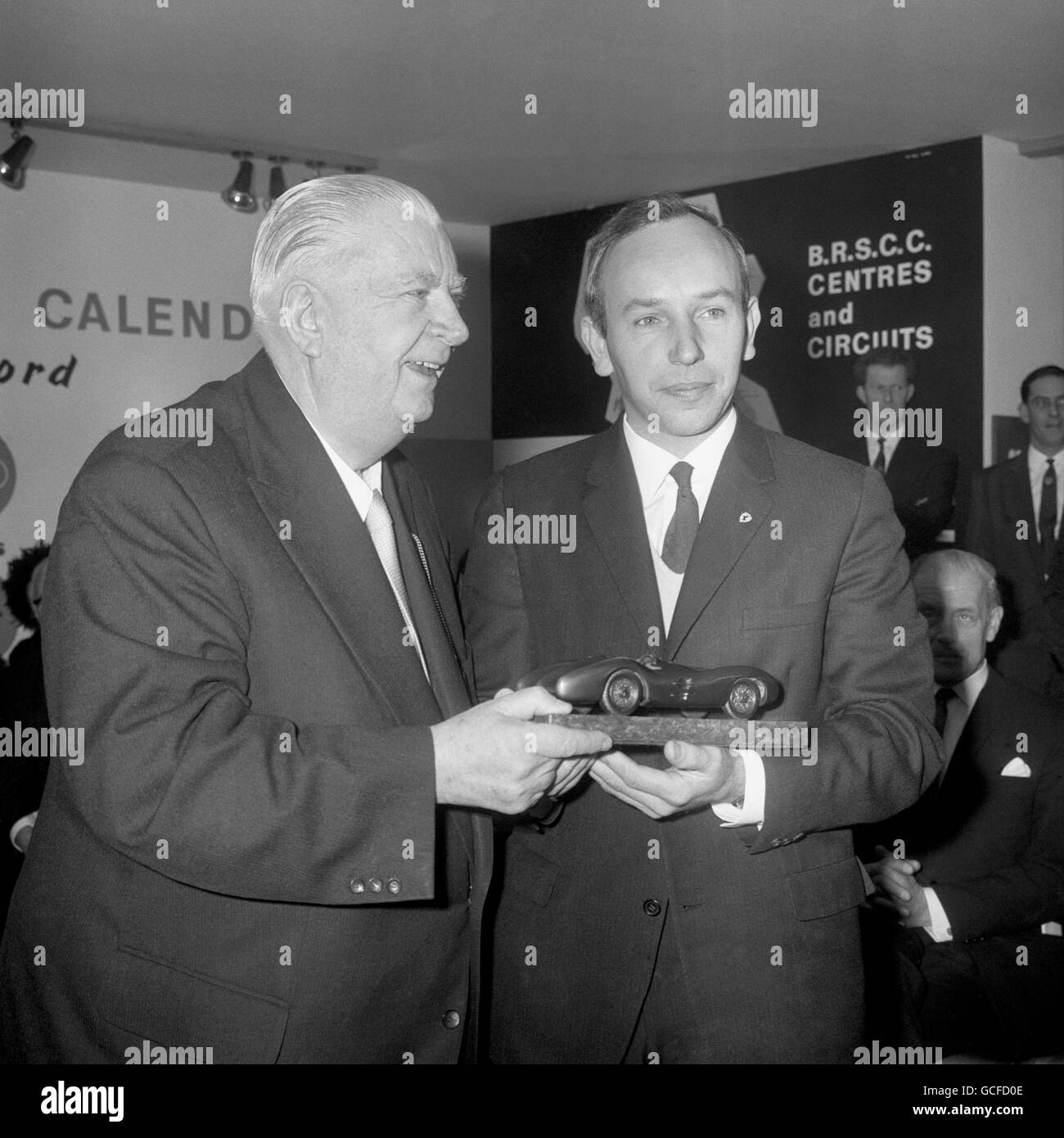 Reigning world champion racing driver John Surtees smiles as, on behalf of the British Racing and Sports Car Club he received a trophy from Herr Alfred Neubauer, team manager of the Mercedes-Benz racing team from 1925 to 1955, when the 6th Racing Car Show opened at Olympia. Stock Photo