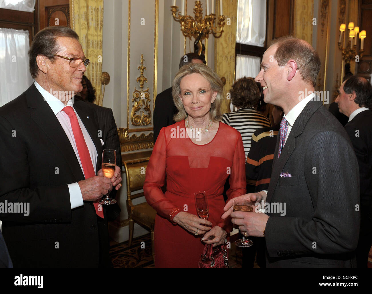 The Earl of Wessex (right) talks with Sir Roger Moore and his wife Kristina, at a drinks reception for the 'Film without Borders' charity at Buckingham Palace in central London. Stock Photo