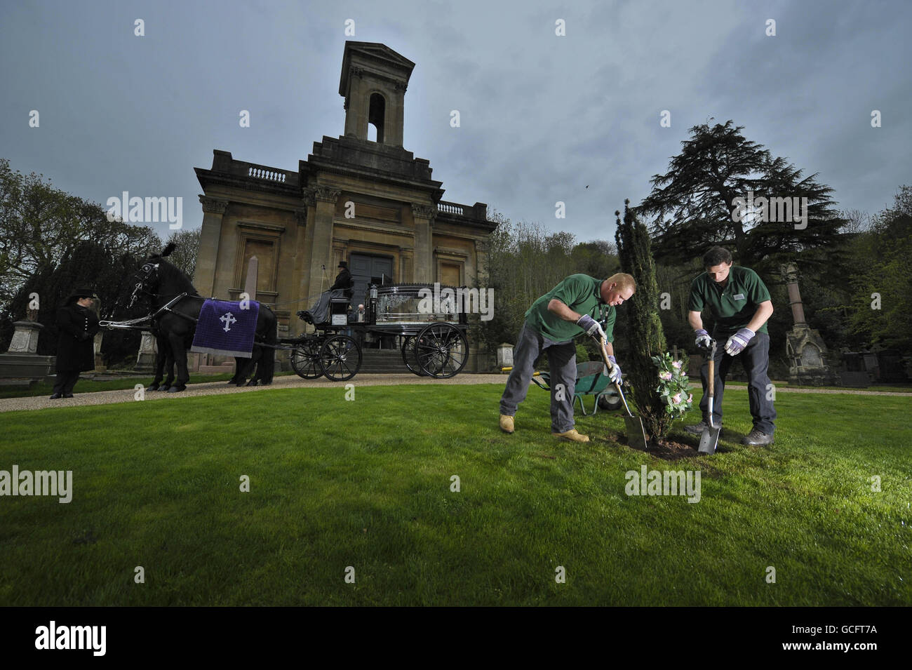 Workmen fill a hole surrounding a new tree in the rain during a ceremony to celebrate the re-opening of the Victorian Arnos Vale cemetery, Bristol, following a 5m project to restore the impressive 45 acre parkland site into a heritage, wildlife, education and visitors centre. Stock Photo