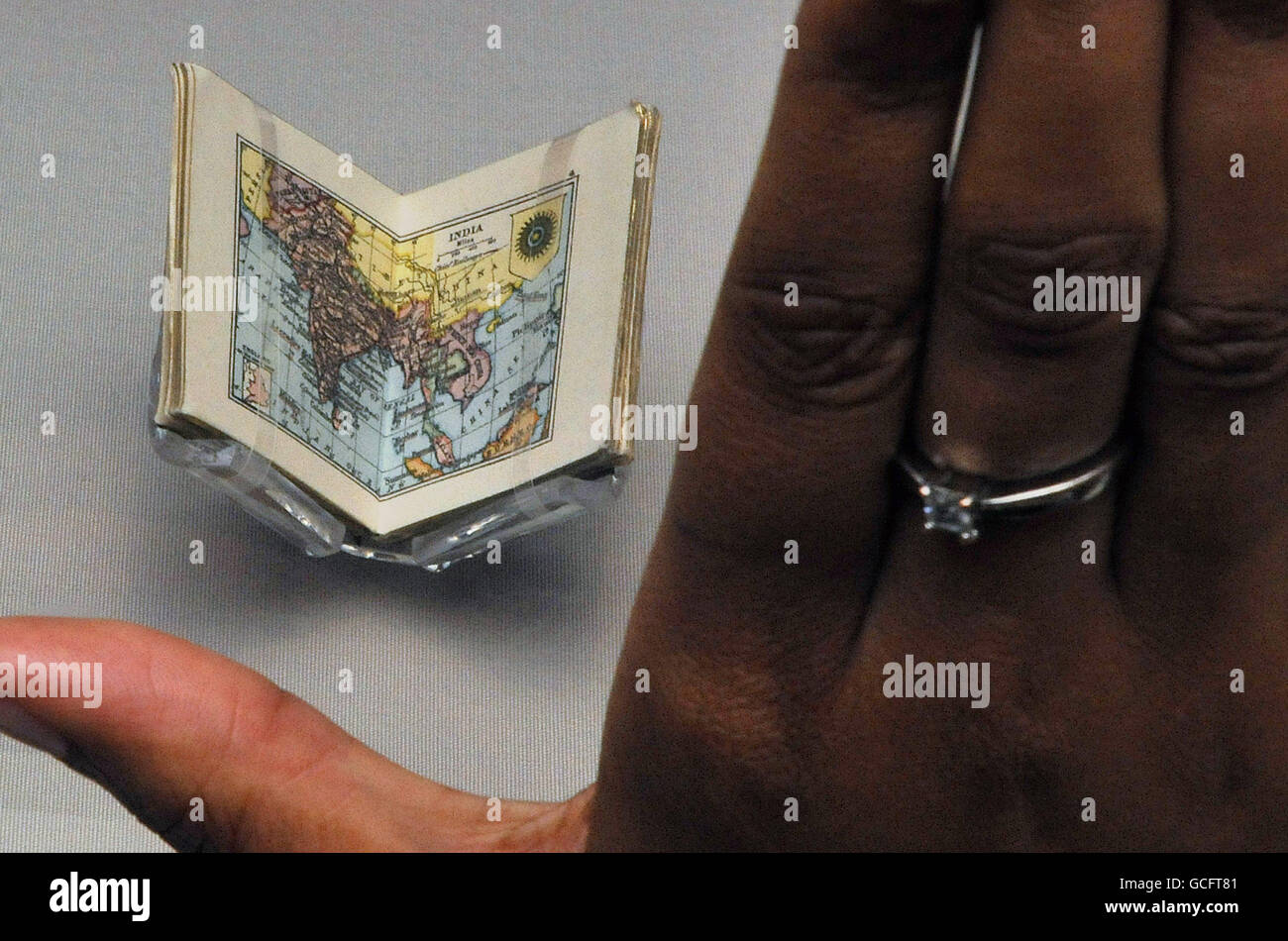 Staff member Radhika Dandeniya views the world's smallest atlas ever to be published which was commissioned for the dolls' house of Queen Mary consort to George V of Britain, part of the British Library's Magnificent Maps exhibition. Stock Photo