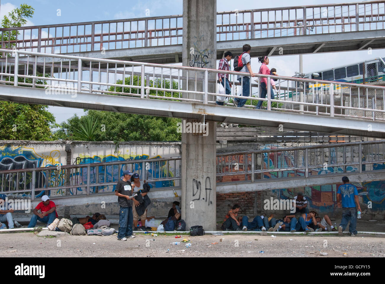 Central American migrants wait below a pedestrian walkway for a passing northbound train to hop, on their journey to the USA. Stock Photo