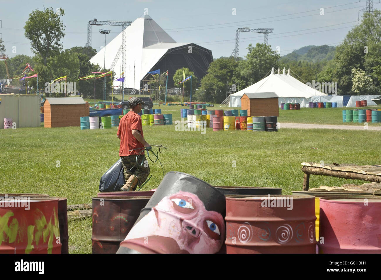 A festival worker tidies fields where the market will be, with the iconic Pyramid stage in the background as the preparations for the Somerset music festival are going well with dry weather and sunny skies on the 1000 acre site at Worthy Farm, Pilton, Somerset. Stock Photo