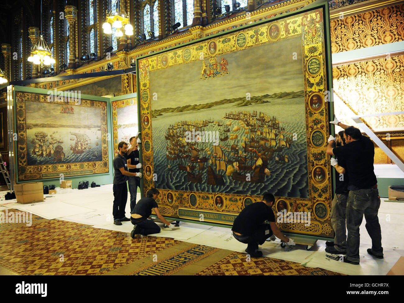 One of six paintings recreating the 'Armada Tapestries', giant gilded canvases depicting the defeat of the Spanish Armada, is inched into place in the Palace of Westminster. The paintings have taken over two years to complete, the original tapestries hung in the House of Lords' chamber for over 200 years before they perished in the 1834 Palace fire. Stock Photo