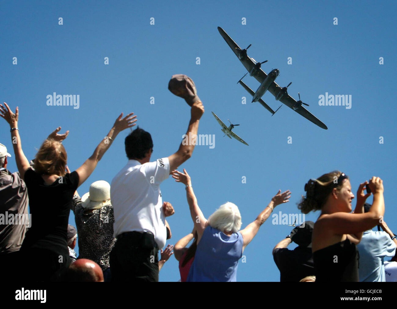 Spectators wave as a Lancaster Bomber and a Spitfire make a flypast over the National Memorial, at Capel-le-Ferne, Kent, as part of an events to mark the 70th anniversary of the Battle of Britain. Stock Photo
