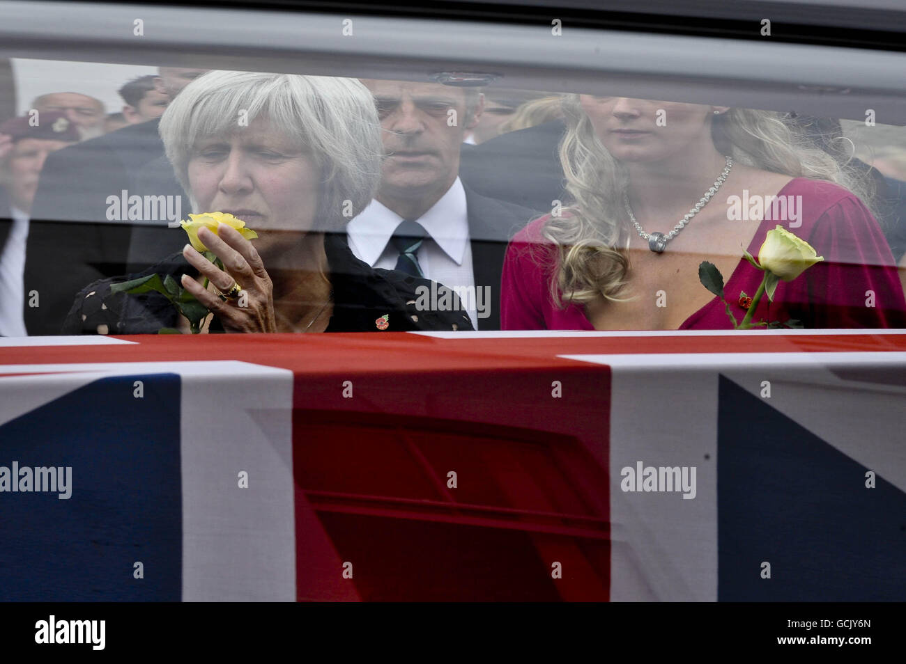 Heidi Kirkpatrick (in the pink dress), the wife of Corporal Jamie Kirkpatrick, 32, of 101 Engineer Regiment, looks on with other mourners as the coffin of her husband is driven along the High Street at Wootton Bassett, Wiltshire. Stock Photo
