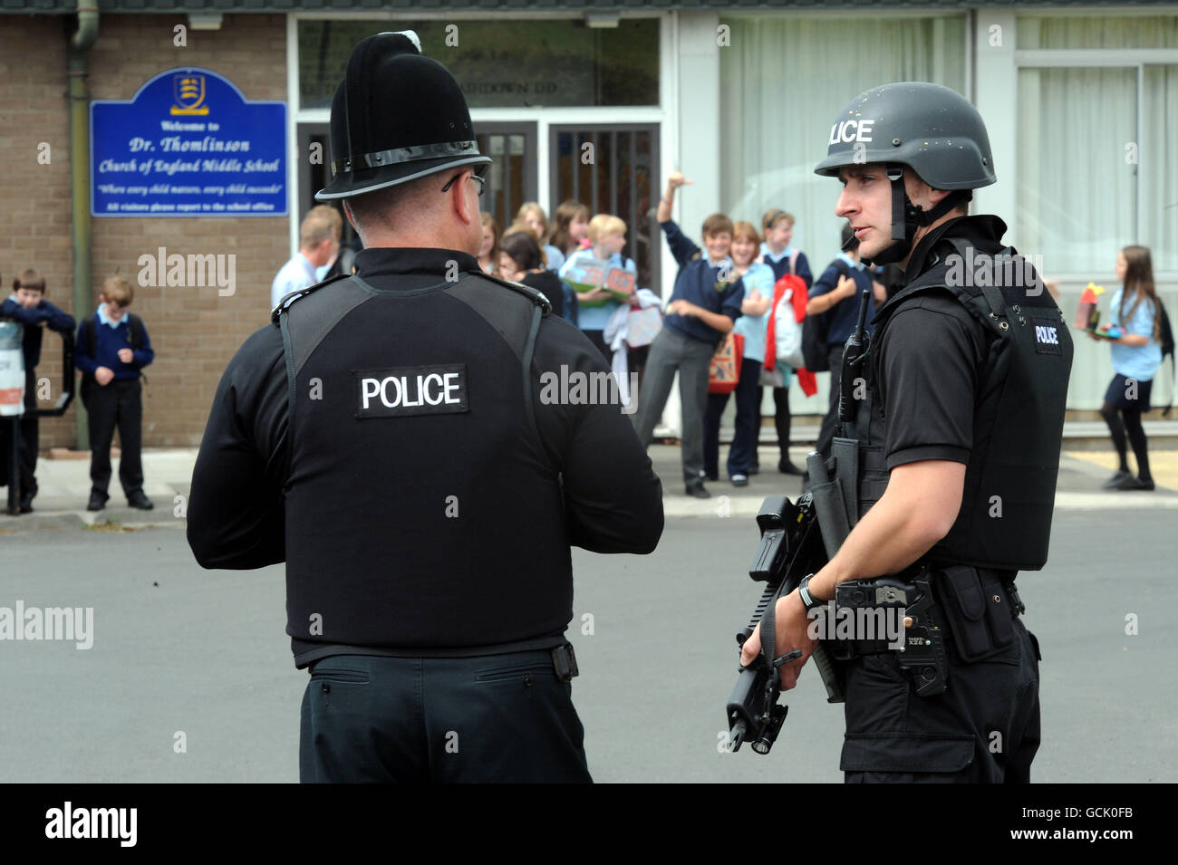 An armed police officer guards the school children leaving Dr