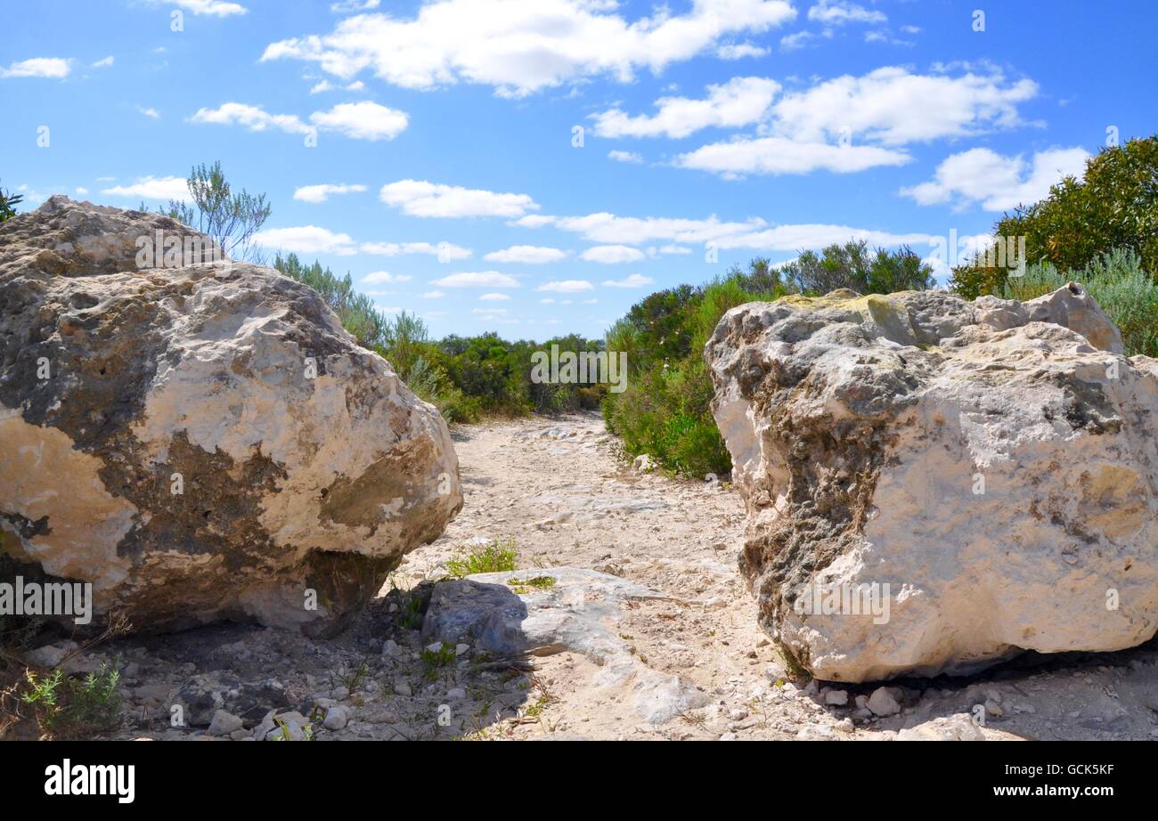Path through two limestone rocks under a blue sky with clouds with ...