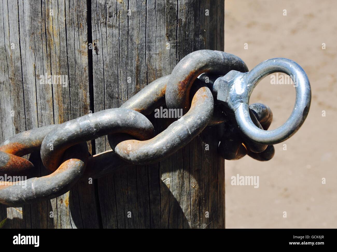 Closeup abstract of rusted chain link with eye-bolt draped against a wooden post. Stock Photo