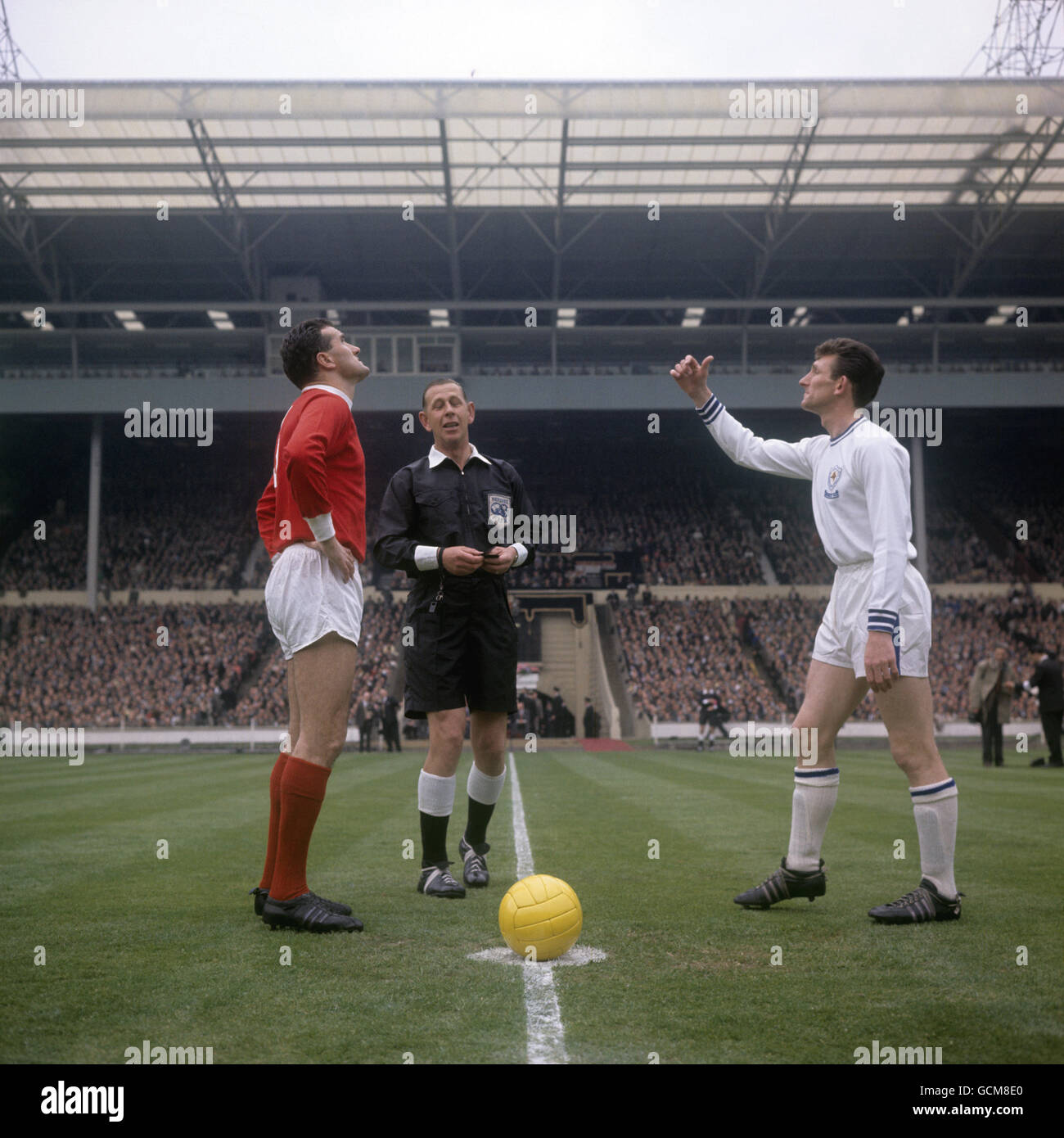 Referee Ken Aston, centre, looks on as captains Noel Cantwell of Manchester United, left, and Leicester City's Colin Appleton toss the coin before the start of the match Stock Photo