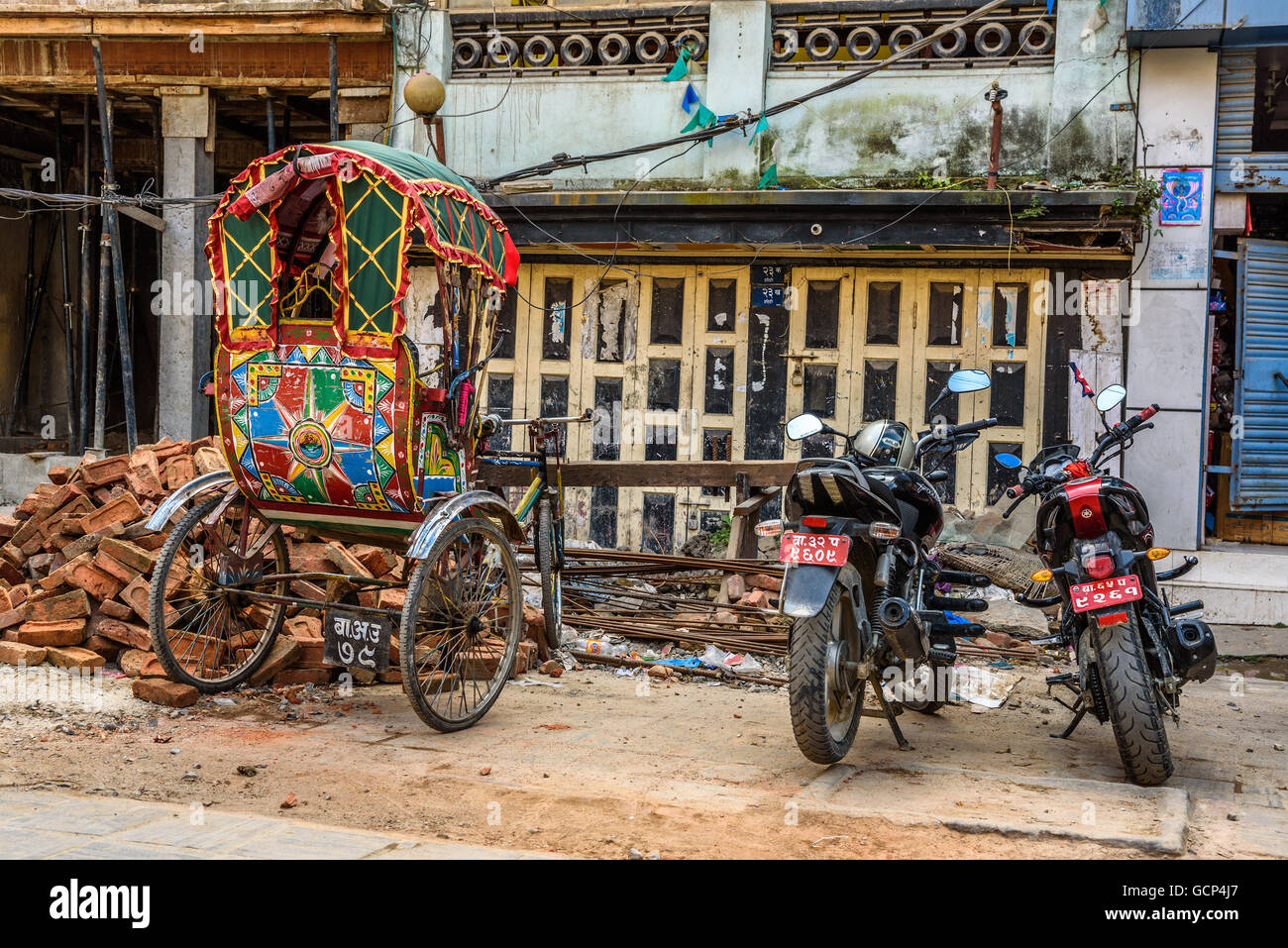 Traditional nepalese rickshaw and motorcycles parked in front of houses damaged by earthquake Stock Photo