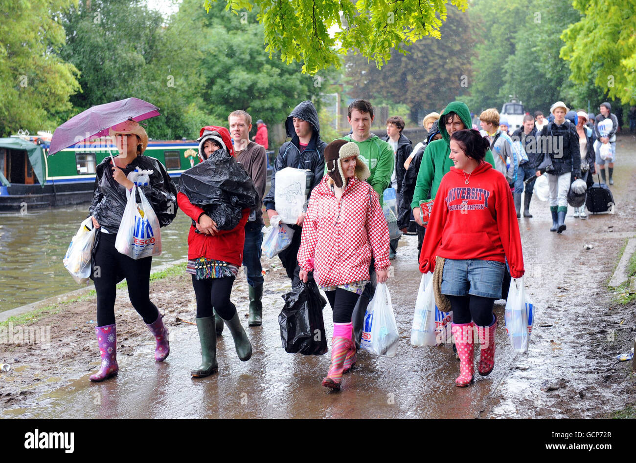 Reading Festival-goers make their way along a muddy Thames towpath from the drop point in the town to the site venue where they will set up camp for the music event this Bank Holiday weekend. Stock Photo