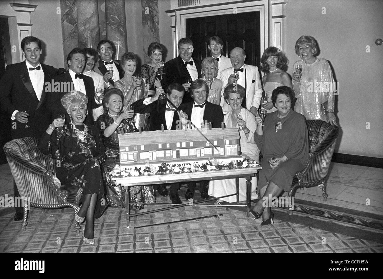 Members of the cast of ITV's soap opera Coronation Street, crowded around a cake replica of the street at the celebration to mark its 25th anniversary at the Dorchester Hotel. Front row, left to right, Julie Goodyear, Eileen Derbyshire, series creater Tony Warren, William Roache, Jean Alexander and Betty Driver. Back row, left to right, Nigel Pivaro, Johnny Briggs, Michael Le Vell, Bill Tarmey, Thelma Barlow, Anne Kirkbride, Bryan Mosley, Lynn Perry, Kevin Kennedy, Bill Waddington, Helen Worth and Liz Dawn. Stock Photo