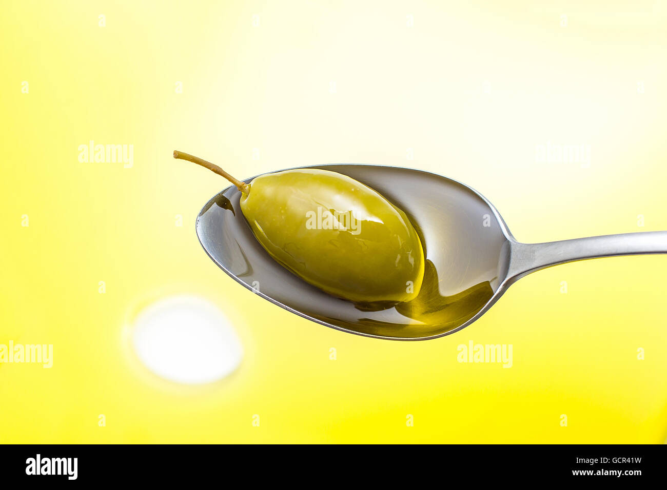 Green olive in full oil spoon on gold background, top view Stock Photo