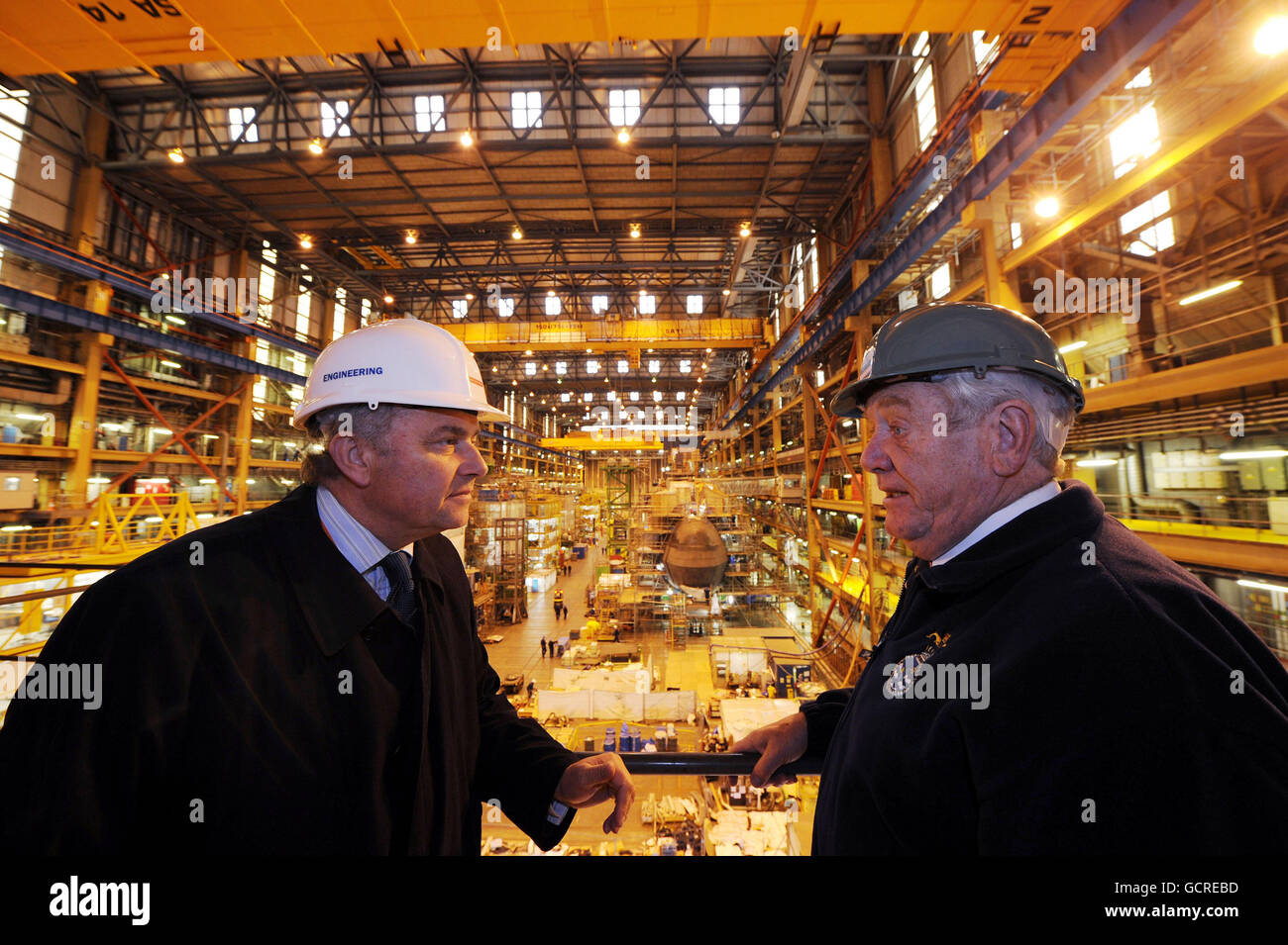 Terry Spurling (right) a former engineer officer of the watch who served on HMS Dreadnought for more than seven years and Tony Burbridge who works on the Astute class subs, stand near the construction of the Ambush submarine at the BAE Systems in Barrow-in Furness. Stock Photo