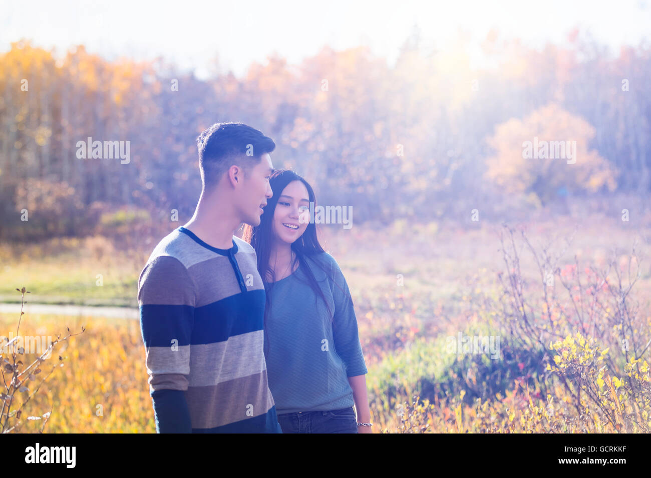 A young Asian couple holding hands while walking in a park in autumn ...