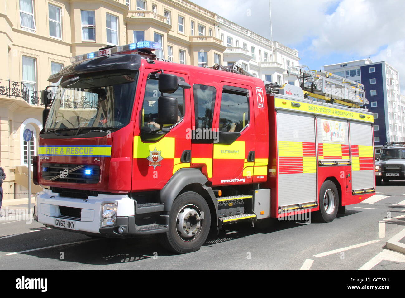 AN EAST SUSSEX FIRE & RESCUE SERVICE VOLVO FIRE TRUCK PASSING ALONG A MAIN ROAD WITH BLUE LIGHTS FLASHING Stock Photo
