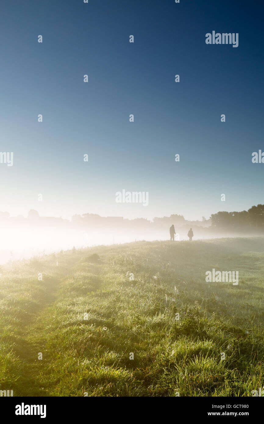 Couple enjoy a misty morning stroll on embankment of the River Derwent at Bubwith , East Riding of Yorkshire, England, UK Stock Photo