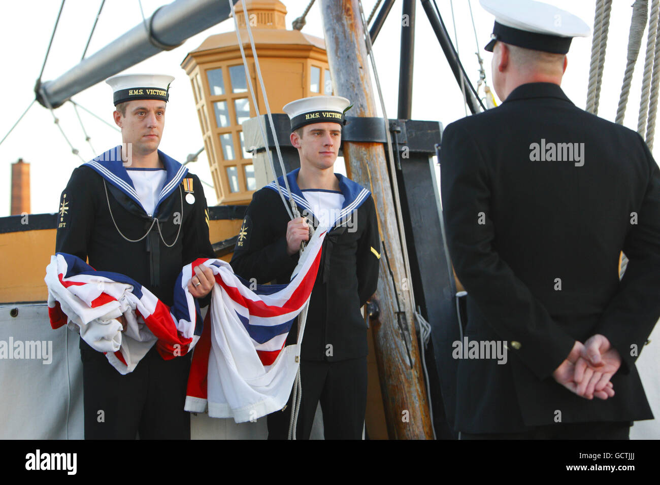 Two Ratings wait to raise the white ensign at the stern of HMS Victory in Portsmouth for morning 'signals,' a daily ritual which all vessels and bases carry out simultaneously each morning and evening. Stock Photo