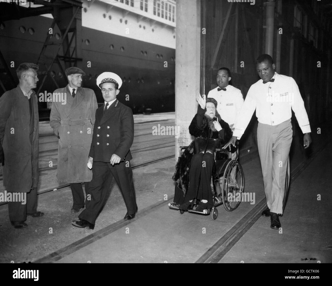 Imperiously, Dame Edith Sitwell waves away photographers as she is wheeled from the liner 'SS United States' on arrival at Southampton. Dame Edith, 69, sprained an ankle in a fall in her New York hotel. With her brother, Sir Osbert, she has been touring the United States giving joint readings of their poetry. Stock Photo