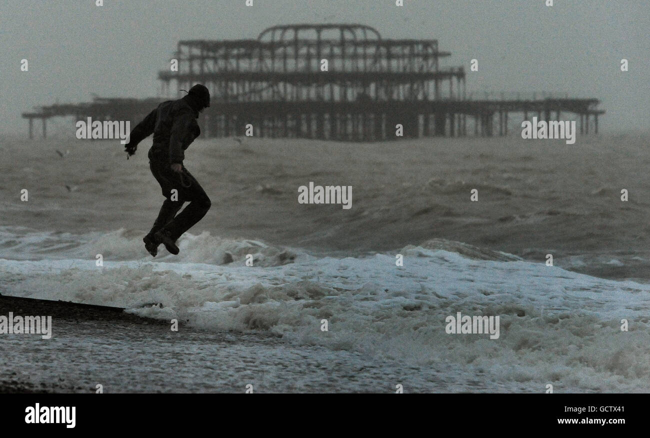 A man jumps on a groyne as heavy wind and rain hits the sea front at Brighton. Stock Photo