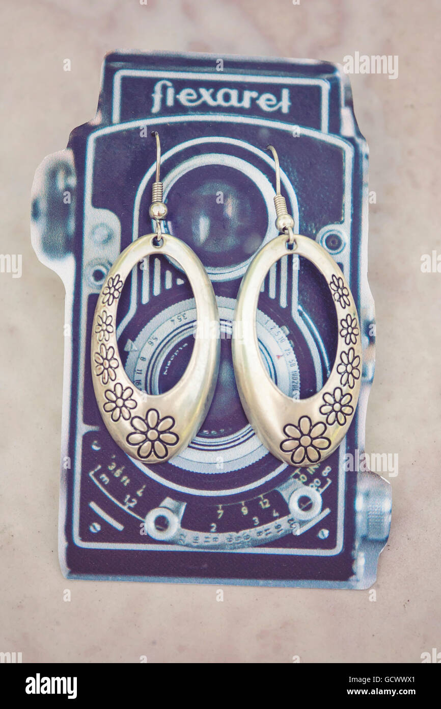 Cute silver earrings with floral motive on funny vintage camera gift card Stock Photo
