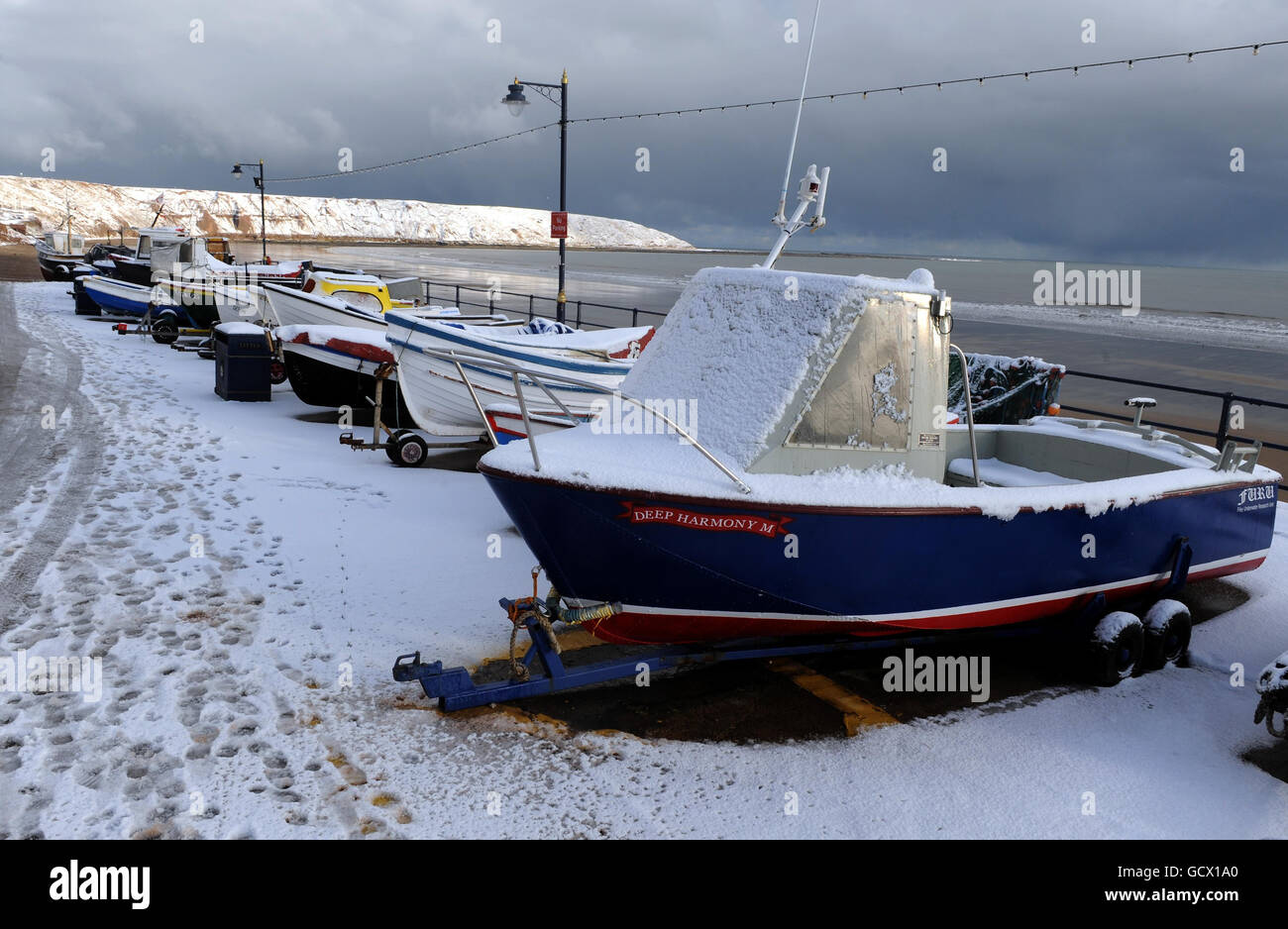 Fishing boats sit covered in snow on the beach in Filey, North Yorkshire, as more snowfalls are forecast along the east coast of the UK. Stock Photo