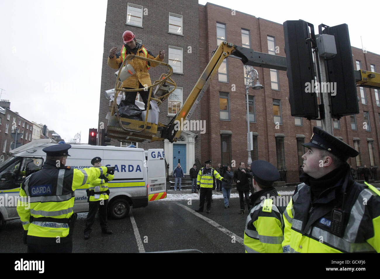 A man uses a cherry picker covered with a number of slogans attacking politicians and the banking sector to protest outside the gates of Leinster House, Dublin, converses with gardai on Budget day. Stock Photo